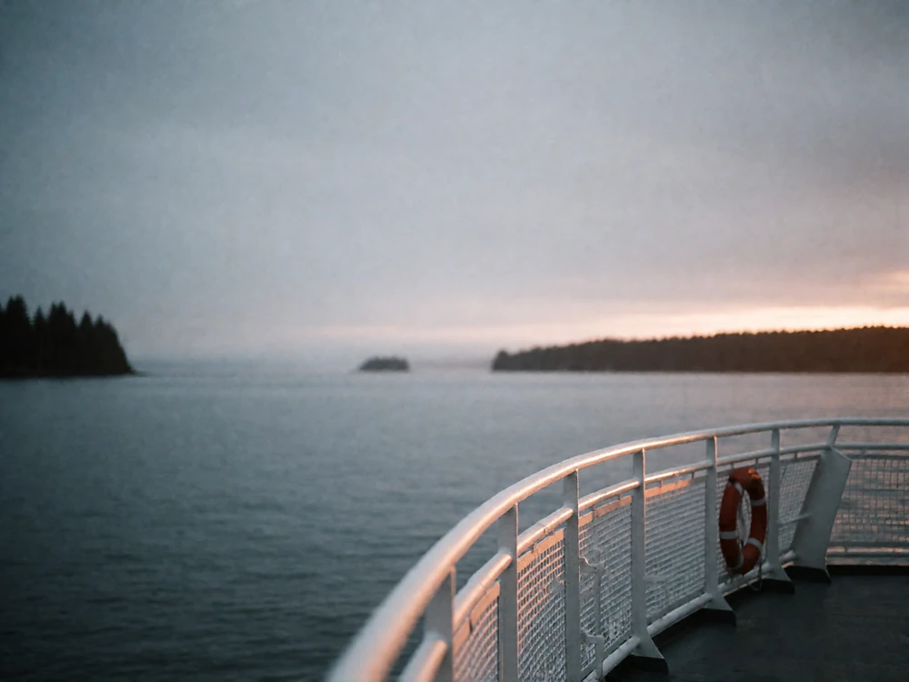 Open deck of a Puget Sound ferry at overcast evening with a rail and distant sunset light