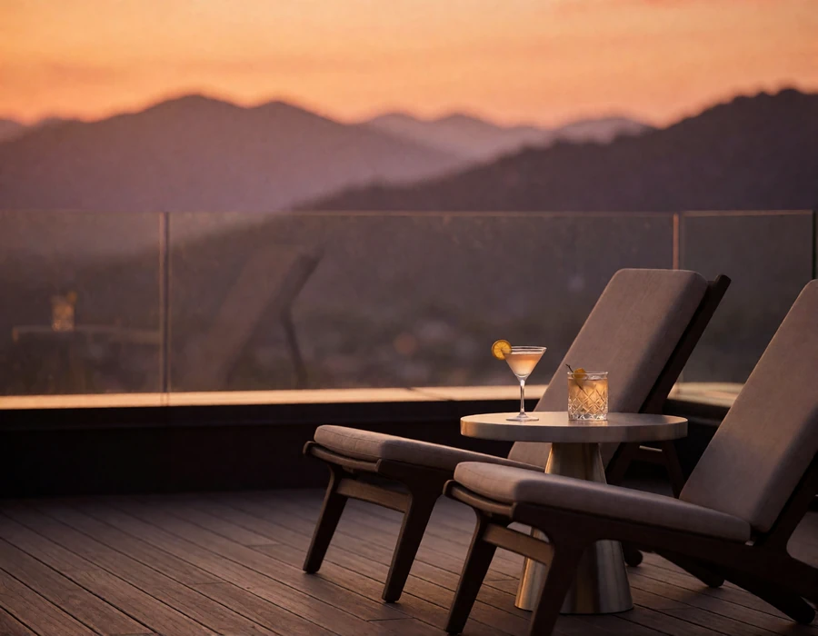 Rooftop terrace lounge chairs and cocktails overlooking layered mountain silhouettes at sunset
